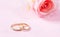 Close up view of golden wedding rings and a blurry pink rose, copy space, on a pink background.