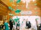 The close-up view of the green paper swans hanging on the ceiling at the blurred background of the guests and newlyweds.