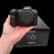 Close up view of hand holding new Canon EOS R5 camera near package box on black background.