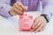 Close up view of the hand of a man placing a coin into the slot of a piggy bank