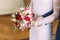 Close-up view of the hands of the bride holding the colouful bouquet of roses and different herbs.