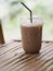 Close up view of ice cubes in cold brewed coffee Cappuccino in plastic cup put on bamboo wooden desk blurred background, drink