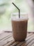 Close up view of ice cubes in cold brewed coffee Cappuccino in plastic cup put on bamboo wooden desk blurred background, drink