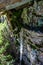 Close up view of an icicle under a rock with moss and lichen