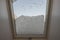 Close up view of interior of snow-covered dormer window on roof of house from room covered with snow on frosty winter day.