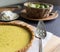 Close up view of a key lime pie with fresh zest on parchment with antique silver pie server. Whipped cream in the background.