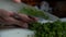 Close up view of knife cutting multiple chives into pile of small vegetable pieces. Preparing green vegetables on the