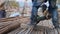 Close-up view of legs in foreground of a worker, cutting pipes with a saw blade.