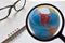 Close-up view, Magnifying glass with a world map. On the desk there are glasses and white books is elements.