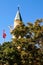 Close-up view minaret which is covered by green tree leaves. Blue sky background. Turkish flag near the minaret