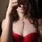 Close up view of mysterious long-haired lady in red brassiere with small key on lace in hand. Selected focus on key