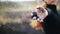 Close-up view of nice girl standing in field in black sweater holding burnt grass in outstretched hand and slowly