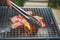 Close up view of pieces of sliced beef on charcoal grill at Outdoor party. Human`s hands using meat tongs to grill Multiple slice