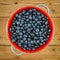 Close-up view of a pile of blueberries in vintage red colander on old wooden floor