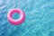 Close-up view of a pink swimming ring in clear sea water with beautiful light pattern on beach.