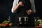 Close-up view of the professional chef in black apron salting water before cooking soup on dark blue background. Backstage of