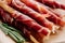 Close up view of rosemary and delicious sliced prosciutto wrapped around breadsticks  on brown