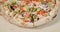 Close-up view of rotating half tasty pizza with bacon and vegetables on light wood background.
