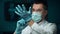 Close up view of serious young bearded man doctor in white professional coat putting on blue protective gloves over lab