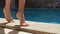 Close up view of slim female tanning barefoot legs careful walking on poolside in spa resort. Woman stepping near pool