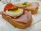 Close up view of stacked sandwich with ham and egg pieces on a white table with blur background