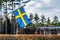 Close up view of Swedish flag with flagpole slowly waving in calm weather. Blurry beautifully colored well trimmed autumn hedges,