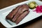 Close up view on tasty brisket beef from smoker on white plate on wooden background. Grilled meat pastrami