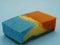 Close up view to the sponge splitted by two colors - blue and orange on the blue background. Used for painting.