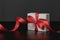 Close-up view of white gift box with elegant red ribbon in luxury bow on dark background and reflection. Gift box with place for t