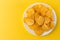 Close-up view on white plate of delicious corrugated golden potato chips fried and salted on a bright yellow background with copy