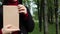Close up view of woman in black woolen coat and burgundy sweater holding a book with empty cover in the park. Free space for your