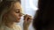 Close-up view of working make-up artist applying eyeshadow to eyelids of woman.