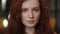 Close up view of young red haired woman turning head and looking to camera. Portrait of seductive female person with