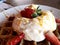 Close up waffles with cream and strawberries on white plate