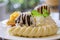 close up waffles served with mixed fruits, sliced banana, ice-cream and topped with chocolate Sauce