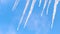 Close up of water dripping from icicles on blue sky background with floating clouds. Concept. Global warming and