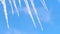 Close up of water dripping from icicles on blue sky background with floating clouds. Concept. Global warming and