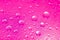 Close-up on water drops background on pink surface. Water droplets on glass with reflections in them.