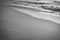 Close up on wave foam of atlantic ocean on sandy beach in black and white