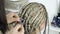 Close-up weaving of light blond braids on a blurry background of a hairdresser