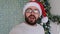 Close-up of a webcam, a portrait of a positive guy, sitting near a decorated glowing holiday tree, congratulates his