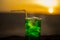 Close up wet glass of green cold mint drink, colorful orange sunset background on the terrace. Cooling summer drink. Summer fresh