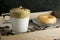 Close up of whipped instant coffee on top of a glass of milk with a doughnut on a wooden tray with coffee beans sprinkled. Dalgona