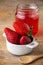 Close-up of white bowl with strawberries, wooden spoon and recycled glass jar with strawberry jelly, on rustic wooden table