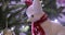 Close-up of white bright fox toy with red scarf, hat hanging on Christmas tree decorated with flashing lights, baubles.