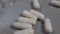 Close-up white capsules spill out of a glass bottle onto a gray plastic surface