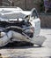 Close up of a white car wrecked during a car accident. Damaged front bumper, engine, headlights