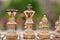 Close up of white chess pieces with focus on queen and king and bishop in straight line and pawns blurred out in background and