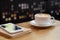 Close up white coffee cup with latte art on wood table with smartphone at coffee shop