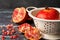 Close-up of white colander with wet pomegranate on blue marble with pieces and pomegranate seeds, dark background